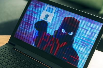 Criminal hiding behind a mask turns up on computer screen asking the owner for money. Concept of phishing and ransomware, where the computer has all files on the harddrive encrypted and the victims need to pay a ransom in order to get their files unlocked.