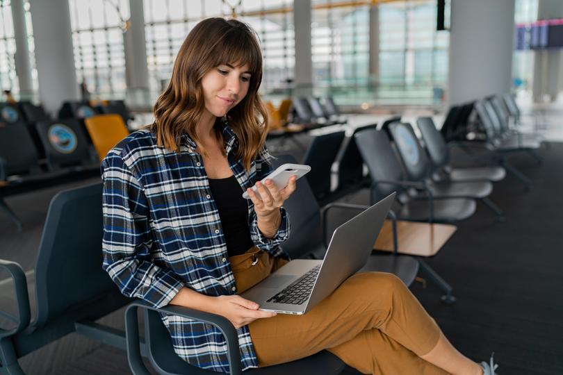 Airport Young female passenger with smart phone and laptop sitting in terminal hall while waiting for her flight