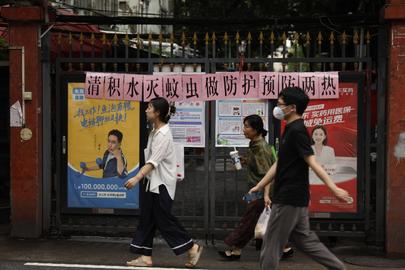 Residents walk past a residential entrance gate displaying a slogan urging mosquito control, in Guangzhou, south China's Guangdong Province, Wednesday, Aug. 6, 2025. The slogan reads "Let's work together to clear stagnant water and eliminate mosquito breeding". (Chinatopix via AP)