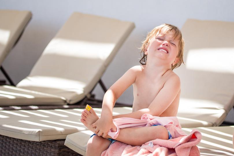 A boy have injured his leg and is crying and suffering pain sitting on a chaise lounge at the beach